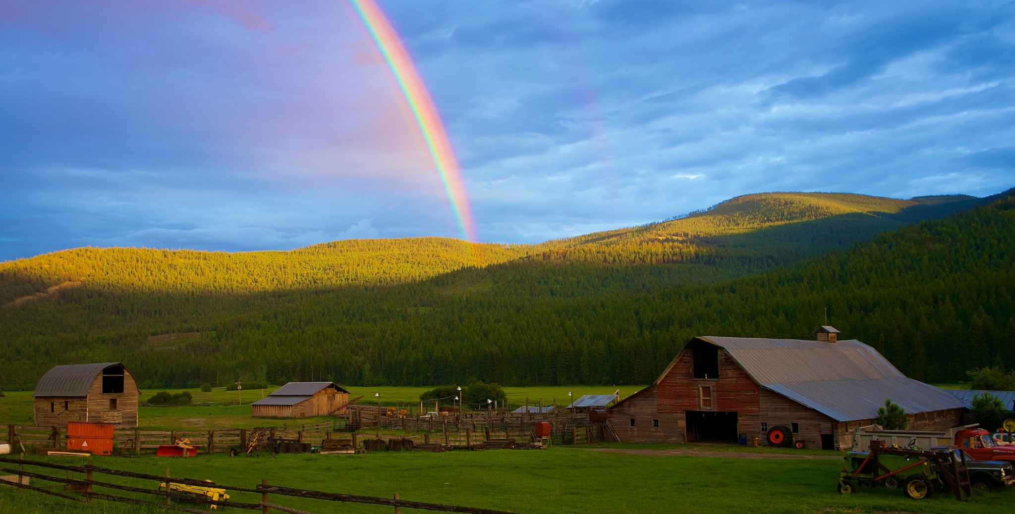 Rural acreage with barns, pasture, forested hills, and a rainbow